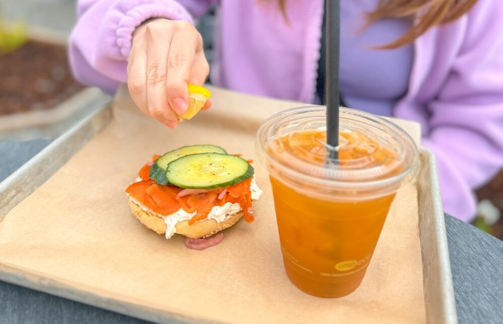 a person squeezing a slice of lemon on a bagel with salmon