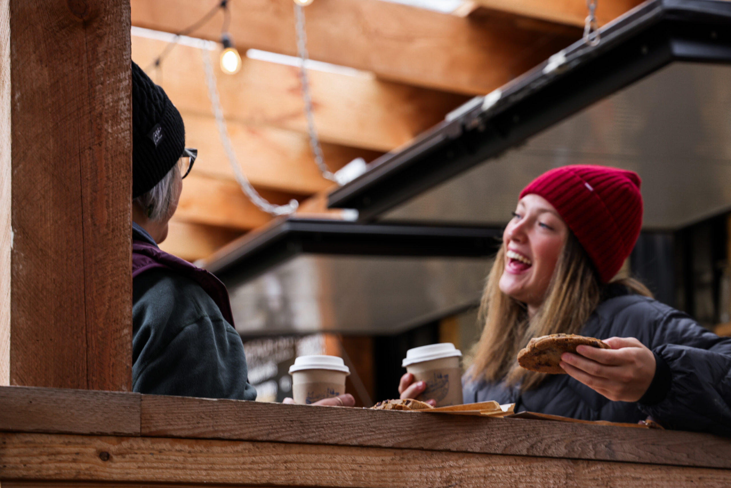 a woman smiling at another woman. they both have a coffee in one hand and one has a cookie in the other hand.