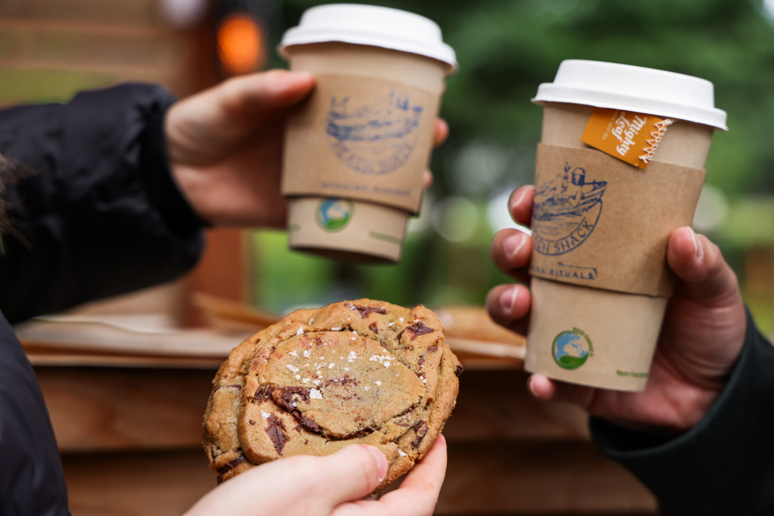 a group of hands holding coffee cups and a cookie