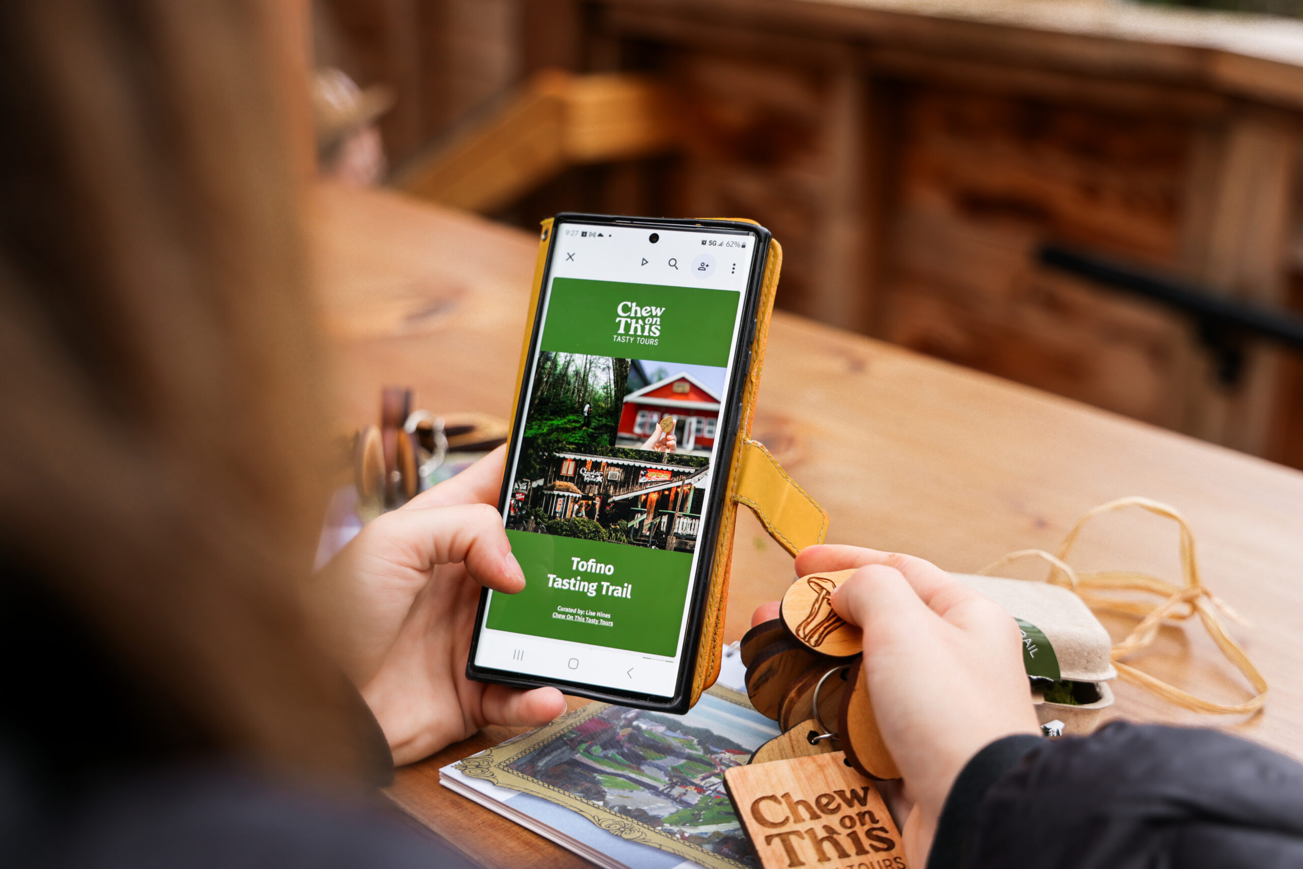 woman holding a mobile phone that is showing the itinerary for the Tofino Tasting Trail.