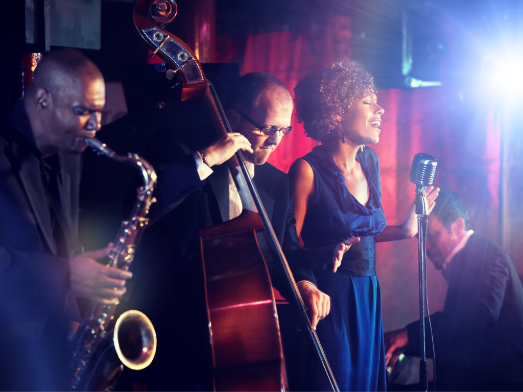 a singer flanked by musicians against a red curtain with moody stage lighting