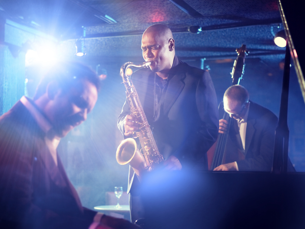 man on stage playing saxophone with man playing piano in foreground.