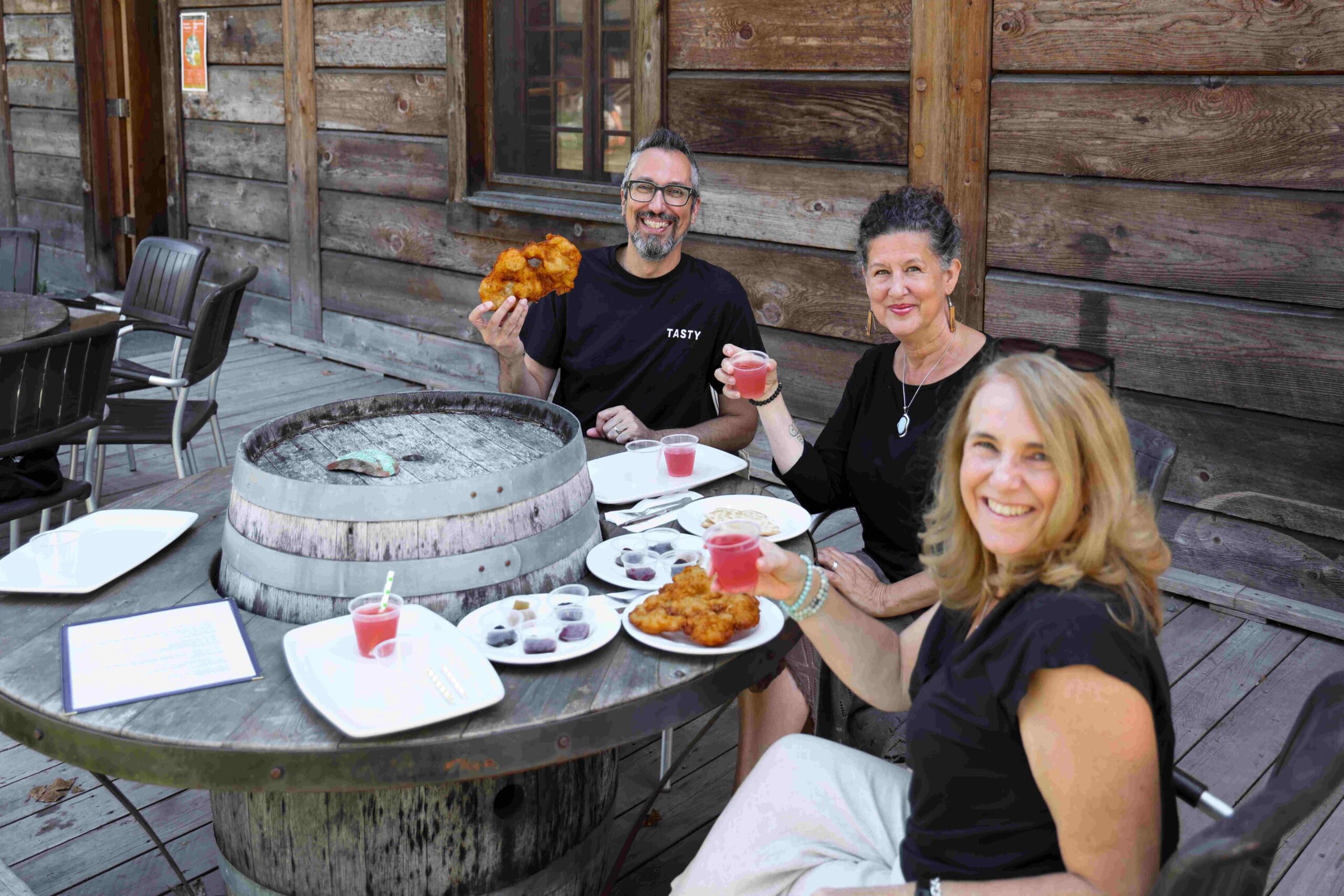 three guests sit around a barrel table with a tasting of bannock and jam and lemonade