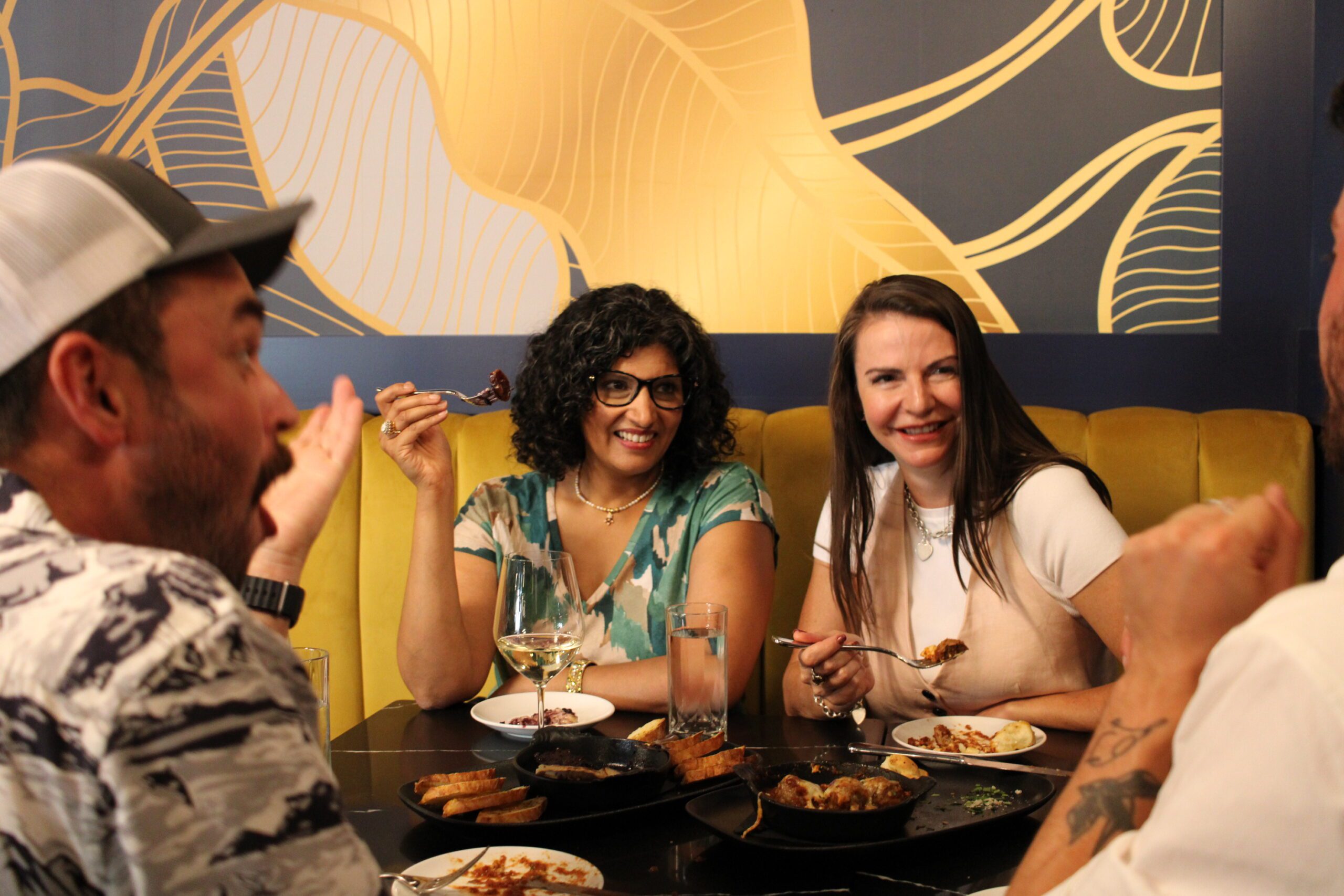 three people laughing at a table with food and wine
